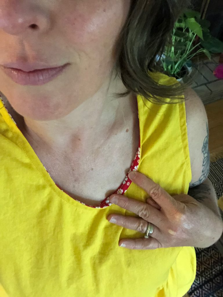I am pulling the neckline of a bright yellow me-made dress to show off the red with daisies bias tape I used