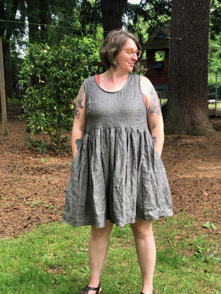I'm looking off into the distance in a brown linen dress with a fullskirt
